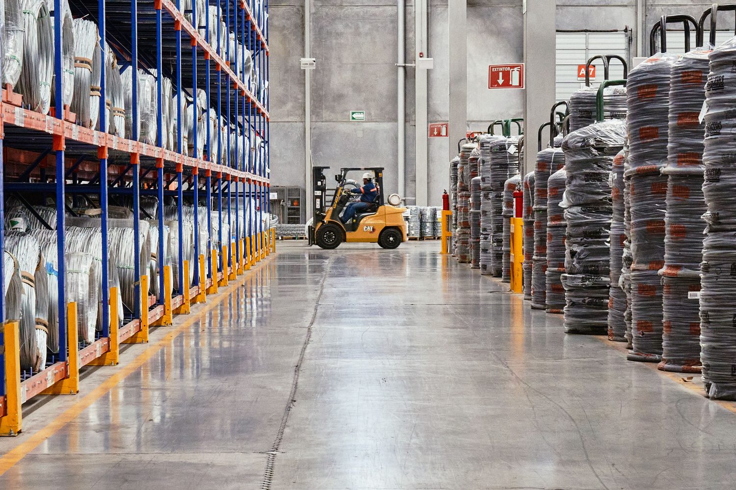 Almacén logístico con estanterías altas y un montacargas trabajando en el pasillo